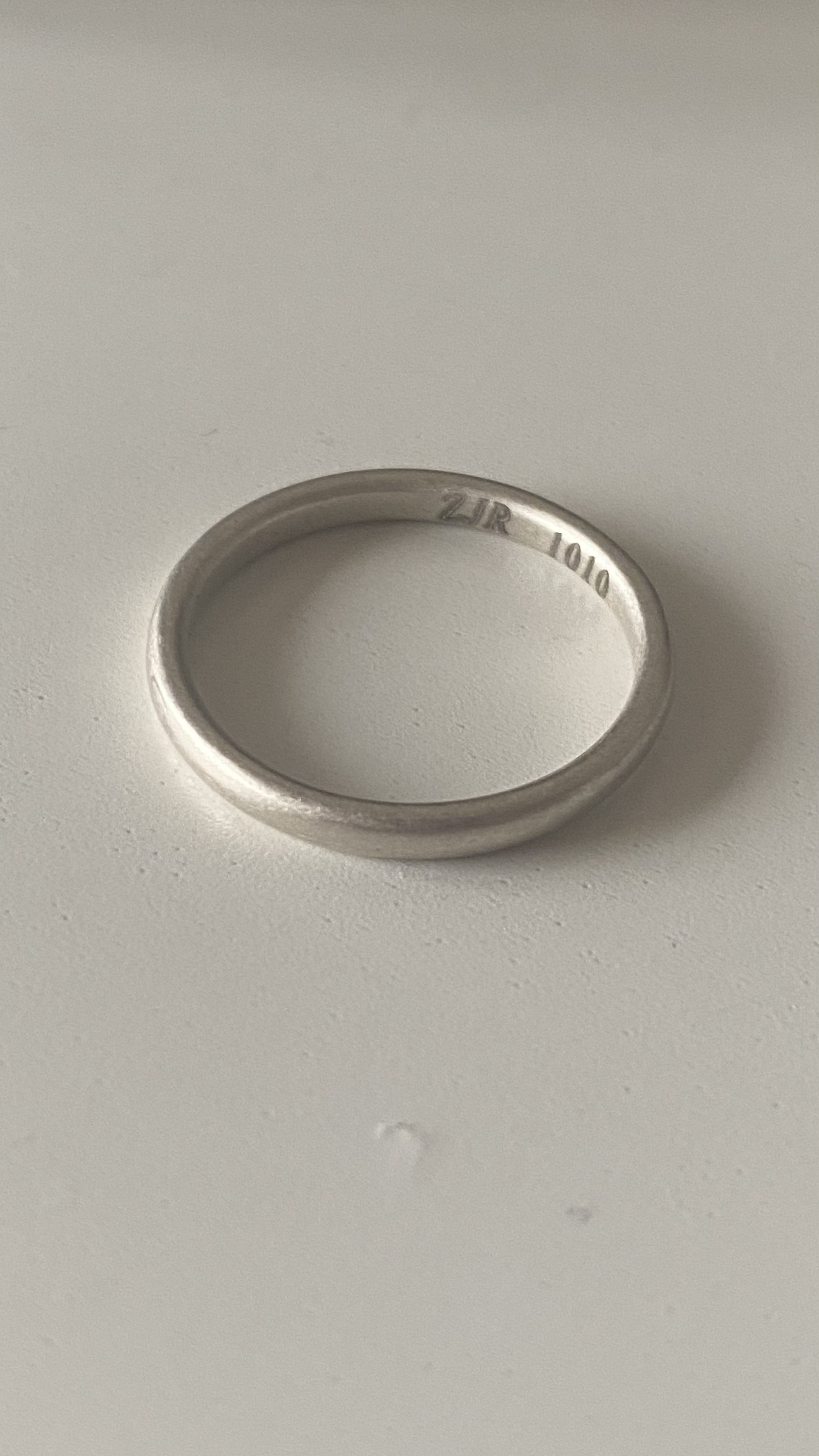 浅色背景上的银色素圈戒指，内侧刻有 ZJR 1010