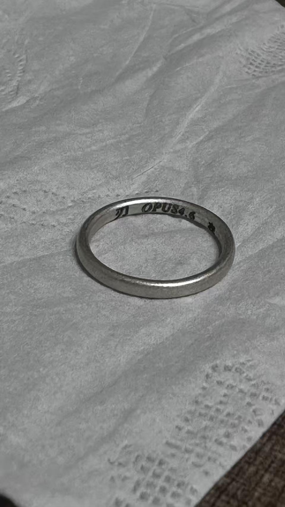 灰色纸面上的银色素圈戒指，内侧刻有刃与 opus4.6